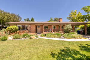 Single story home featuring a chimney, a front yard, brick siding, and a carport