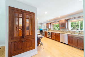 Kitchen featuring appliances with stainless steel finishes, custom cabinetry, light wood-style floors, decorative backsplash, and glass insert cabinets