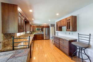 Kitchen featuring stainless steel appliances, glass insert cabinets, tasteful backsplash, light wood-type flooring, and light stone counters