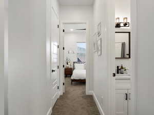 Hallway with dark colored carpet and a chandelier