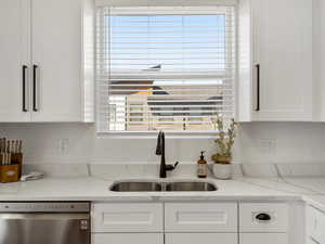 Kitchen with dishwasher, white cabinetry, and light stone countertops