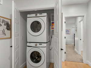 Laundry area with stacked washer and clothes dryer and light wood-style flooring