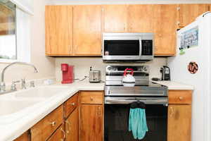 Kitchen with stainless steel appliances, light countertops, brown cabinetry, and tile patterned flooring