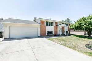 Raised ranch featuring driveway, a garage, a front lawn, and brick siding