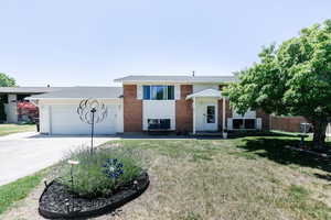 Bi-level home with driveway, a garage, a front lawn, and brick siding