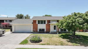Raised ranch featuring an attached garage, concrete driveway, a front yard, and brick siding