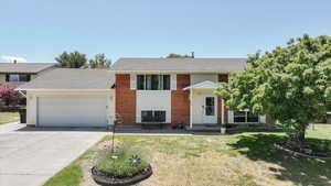 Split foyer home featuring a garage, concrete driveway, and a front lawn