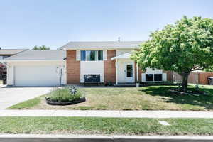 Bi-level home featuring a garage, a front yard, driveway, and brick siding