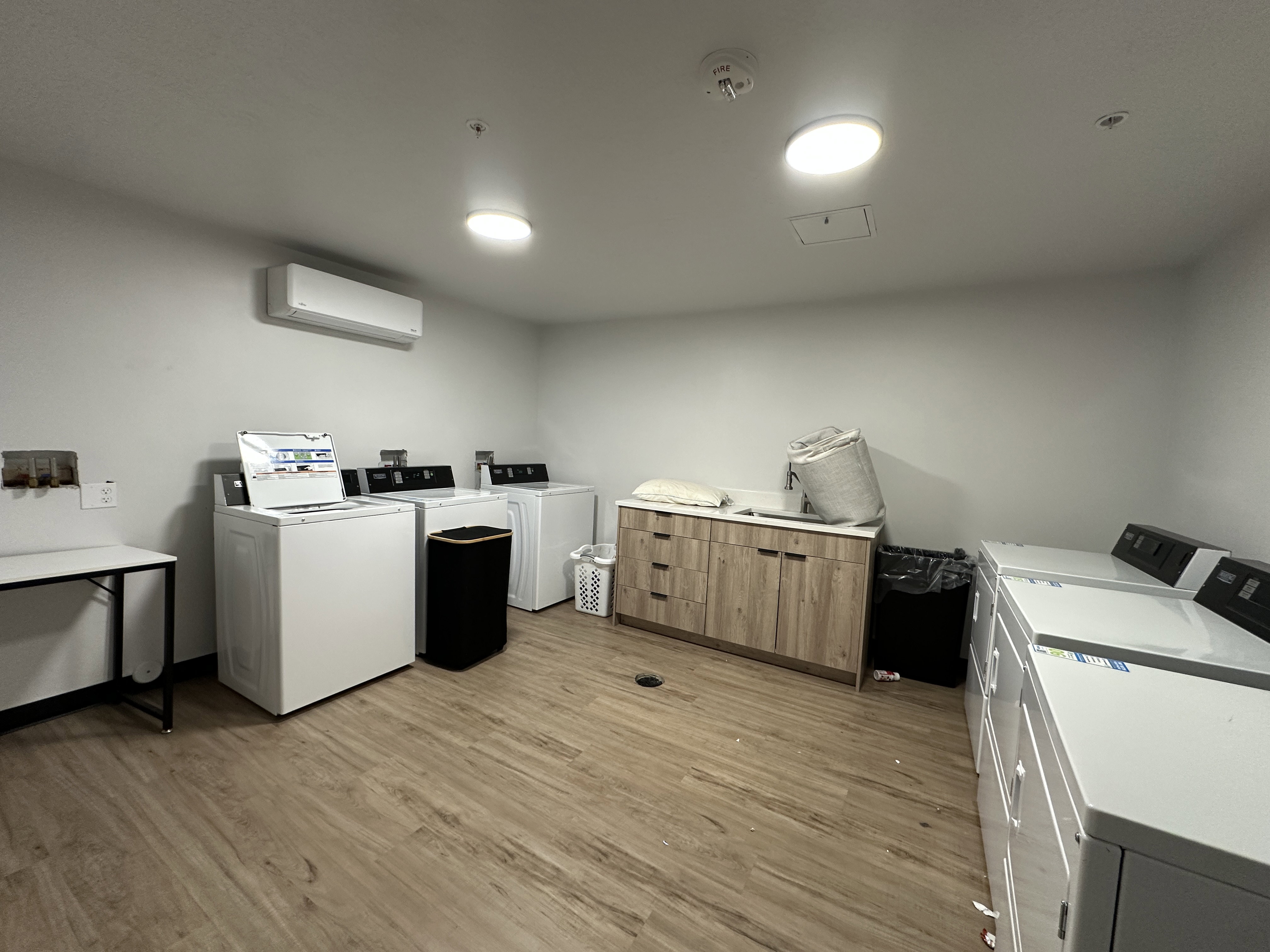 Community laundry with separate washer and dryer, an AC wall unit, and light wood-type flooring