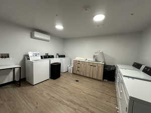 Community laundry with separate washer and dryer, an AC wall unit, and light wood-type flooring