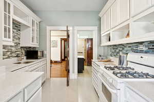 Kitchen with white range with gas stovetop, open shelves, tasteful backsplash, and white cabinetry