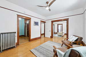 Living area with radiator heating unit, a ceiling fan, and light wood-style floors