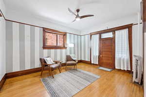 Sitting room featuring light wood-style floors, ceiling fan, and wallpapered walls