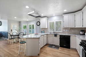 Kitchen with black appliances, a peninsula, white cabinets, light wood finished floors, and recessed lighting