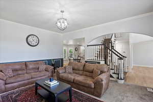 Living room featuring stairway, a chandelier, arched walkways, and ornamental molding
