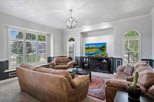 Living room with carpet floors, crown molding, a chandelier, healthy amount of natural light, and a wainscoted wall
