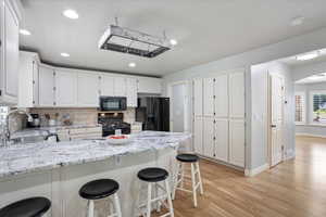 Kitchen with black appliances, a peninsula, light wood-style flooring, white cabinets, and backsplash