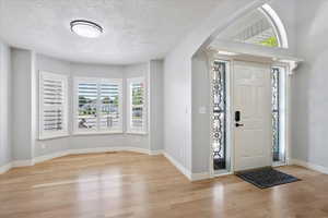 Foyer entrance with wood finished floors, healthy amount of natural light, a textured ceiling, and arched walkways