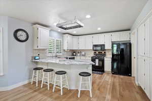 Kitchen featuring black appliances, a peninsula, light wood finished floors, white cabinets, and backsplash