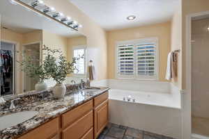 Full bath featuring double vanity, a bath, stone finish flooring, a walk in closet, and a shower stall