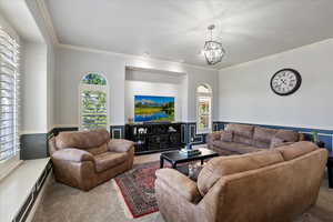 Living room with carpet floors, ornamental molding, healthy amount of natural light, a chandelier, and a wainscoted wall