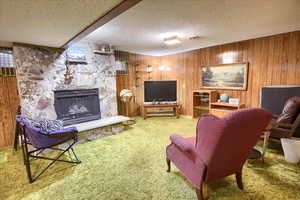 Living room featuring  carpet, a stone fireplace, and wood paneling.