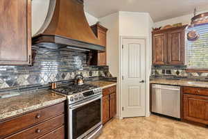 Kitchen featuring stainless steel appliances, custom exhaust hood, backsplash, and dark stone countertops