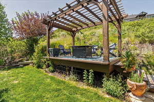 View of grassy yard with a wooden deck and a pergola