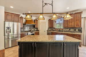 Kitchen featuring appliances with stainless steel finishes, a kitchen island, custom exhaust hood, tasteful backsplash, and recessed lighting