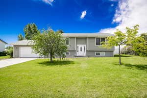 Raised ranch featuring concrete driveway, a front lawn, and a garage