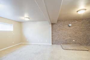Carpeted spare room featuring brick wall and baseboards