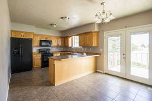 Kitchen with black appliances, plenty of natural light, a peninsula, and a chandelier