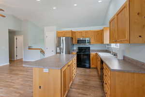 Kitchen featuring black appliances, lofted ceiling, ceiling fan, light wood-type flooring, and a kitchen island