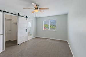Unfurnished bedroom with a spacious closet, a barn door, and carpet flooring