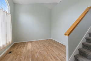 Empty room with stairs, light wood-type flooring, and lofted ceiling