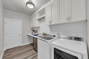 Washroom with cabinet space, washer and dryer, and light wood-style floors