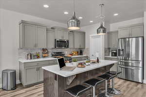 Kitchen with appliances with stainless steel finishes, gray cabinets, light wood finished floors, light countertops, and recessed lighting