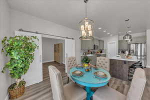 Dining room with a barn door, light wood-style flooring, a chandelier, and recessed lighting
