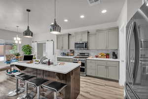 Kitchen featuring appliances with stainless steel finishes, gray cabinets, light wood-type flooring, light countertops, and decorative backsplash