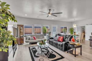 Living room with a ceiling fan, light wood finished floors, a barn door, recessed lighting, and a textured ceiling