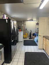 Kitchen featuring black fridge with ice dispenser, washer / dryer, light tile patterned floors, concrete block wall, and stove