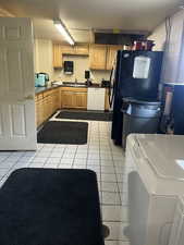 Kitchen with dishwasher, light tile patterned flooring, freestanding refrigerator, and dark countertops