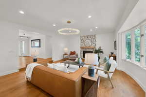 Living area featuring light wood-type flooring, recessed lighting, a chandelier, and a stone fireplace