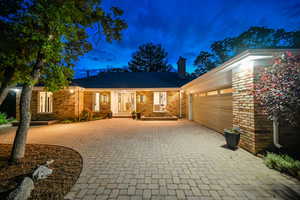 Ranch-style house featuring decorative driveway, a garage, a chimney, and brick siding