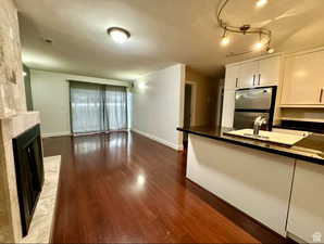 Kitchen featuring freestanding refrigerator, wood finished floors, white cabinets, a tiled fireplace, and dark countertops