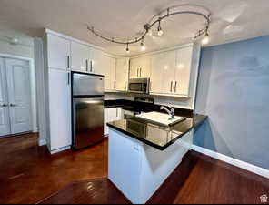 Kitchen featuring appliances with stainless steel finishes, a peninsula, white cabinetry, finished concrete flooring, and a kitchen breakfast bar
