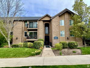 View of front facade featuring a balcony, brick siding, a front yard, and stucco siding