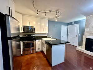 Kitchen featuring stainless steel appliances, a peninsula, white cabinetry, and dark countertops