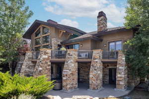 Back of property featuring a balcony, stone siding, and a chimney