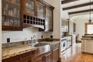 Kitchen featuring beam ceiling, light wood-style floors, high end range, glass insert cabinets, and decorative light fixtures